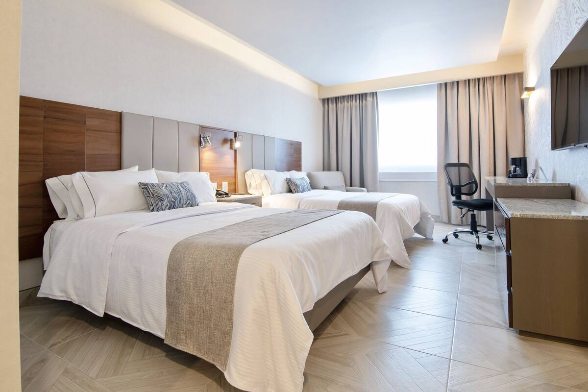 Une chambre d’hôtel avec deux lits, un bureau, une chaise et une grande fenêtre avec des rideaux.