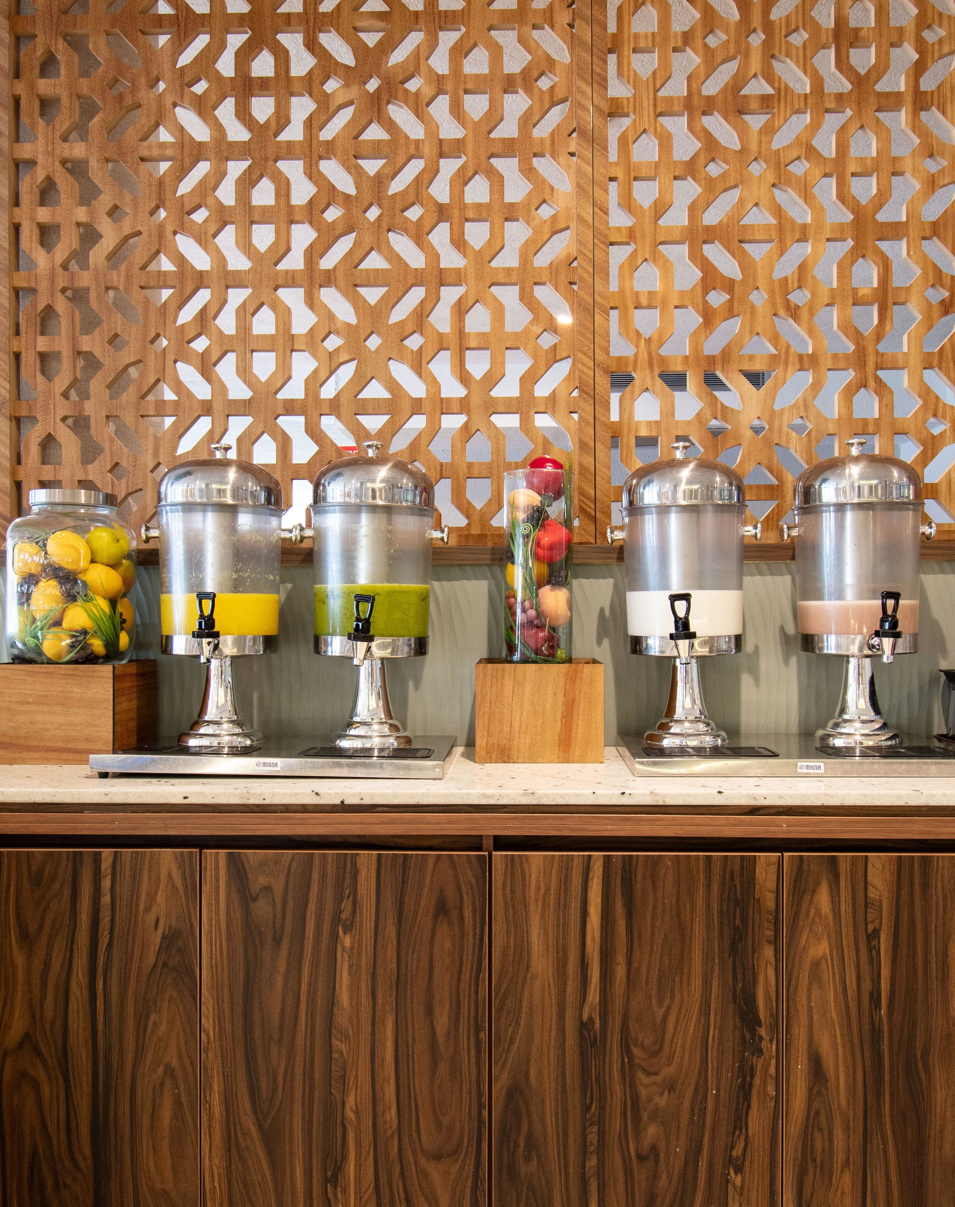 A buffet setup with various food dispensers and a decorative wooden panel in the background.