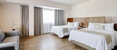 A hotel room with two beds, a sofa, a small table, and a large window with curtains.