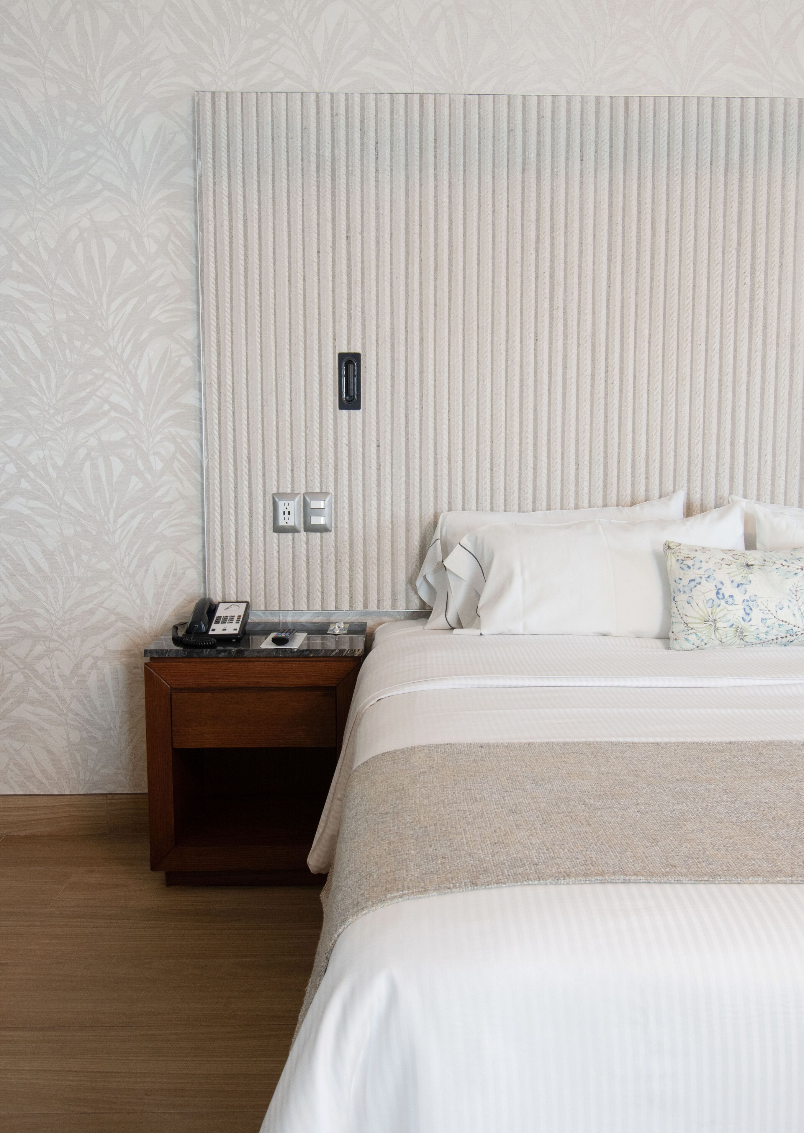 Habitación de hotel con una cama, una mesita de noche, un teléfono y un enchufe en la pared.