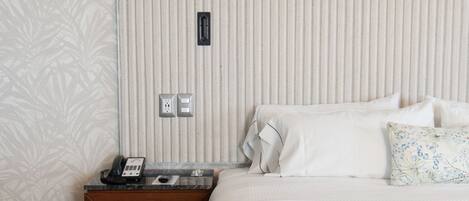 Habitación de hotel con una cama, una mesita de noche, un teléfono y un enchufe en la pared.