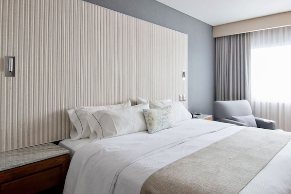 A hotel room with a large bed, a nightstand, a chair, and a window with curtains.