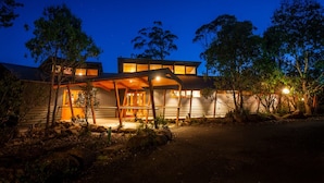 Una casa moderna con porche cubierto, amplias ventanas e iluminación exterior brillante en la noche.