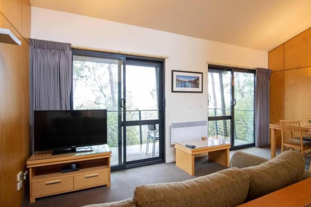 Ein modernes Wohnzimmer mit Flachbildfernseher, einer Couch, einem kleinen Tisch und einem Essbereich mit Stühlen.