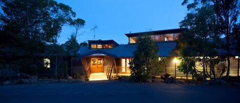 A modern two-story house with a reception area, large windows, and a well-lit driveway.
