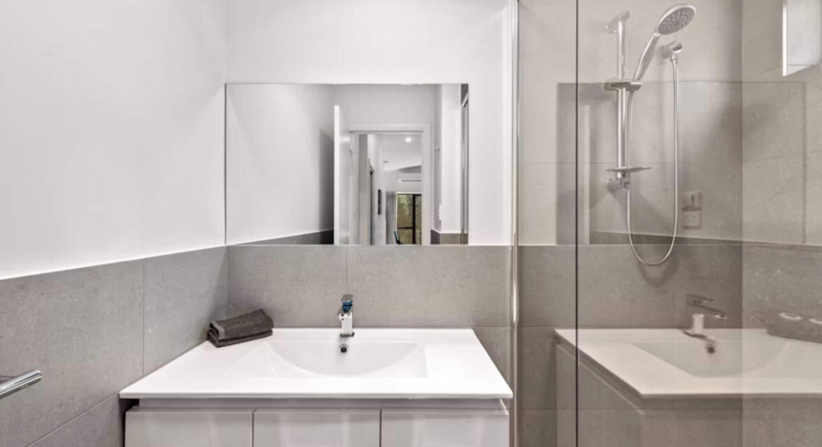 A modern bathroom with a large mirror, a shower, and a sink.
