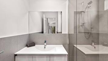 A modern bathroom with a large mirror, a shower, and a sink.