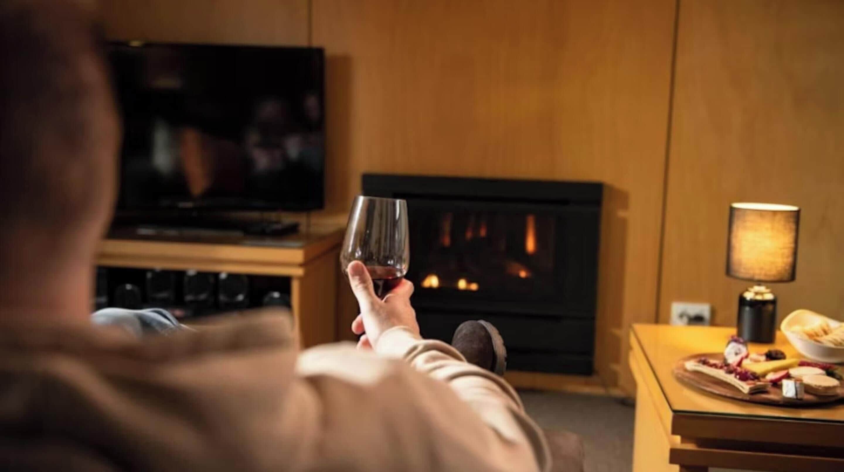 Una persona sosteniendo un vaso en una habitación con chimenea, televisor y una mesa con comida.