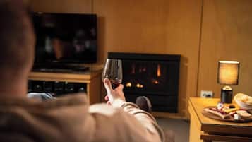 Una persona sosteniendo un vaso en una habitación con chimenea, televisor y una mesa con comida.