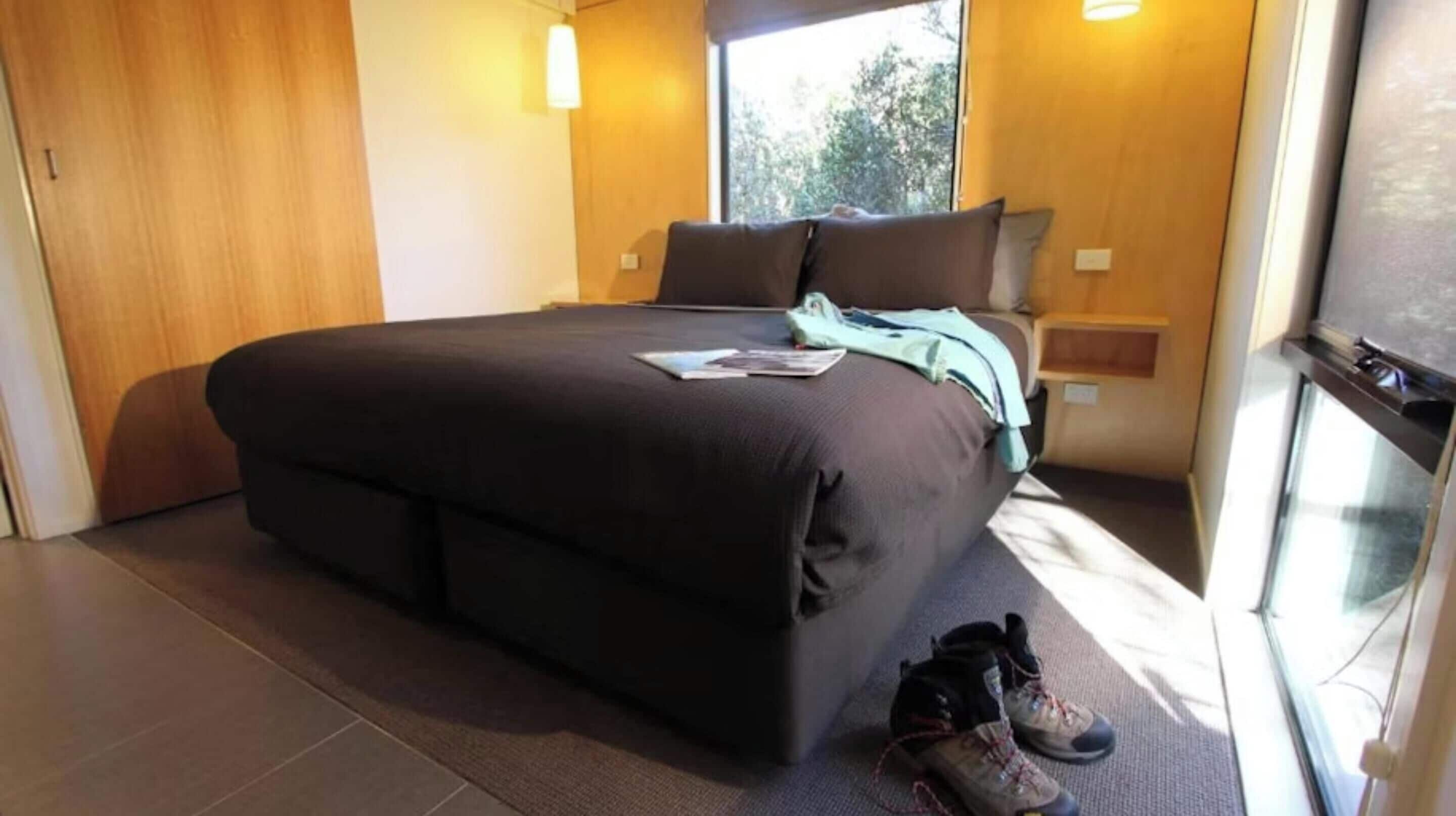 Une chambre avec un grand lit, une table de chevet, une fenêtre et une paire de chaussures sur le sol.