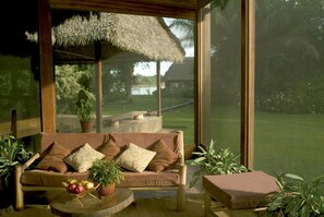 A cozy room with a large window, a thatched roof, and a view of a grassy area and a building. - Inkaterra Reserva Amazonica (Las Piedras)