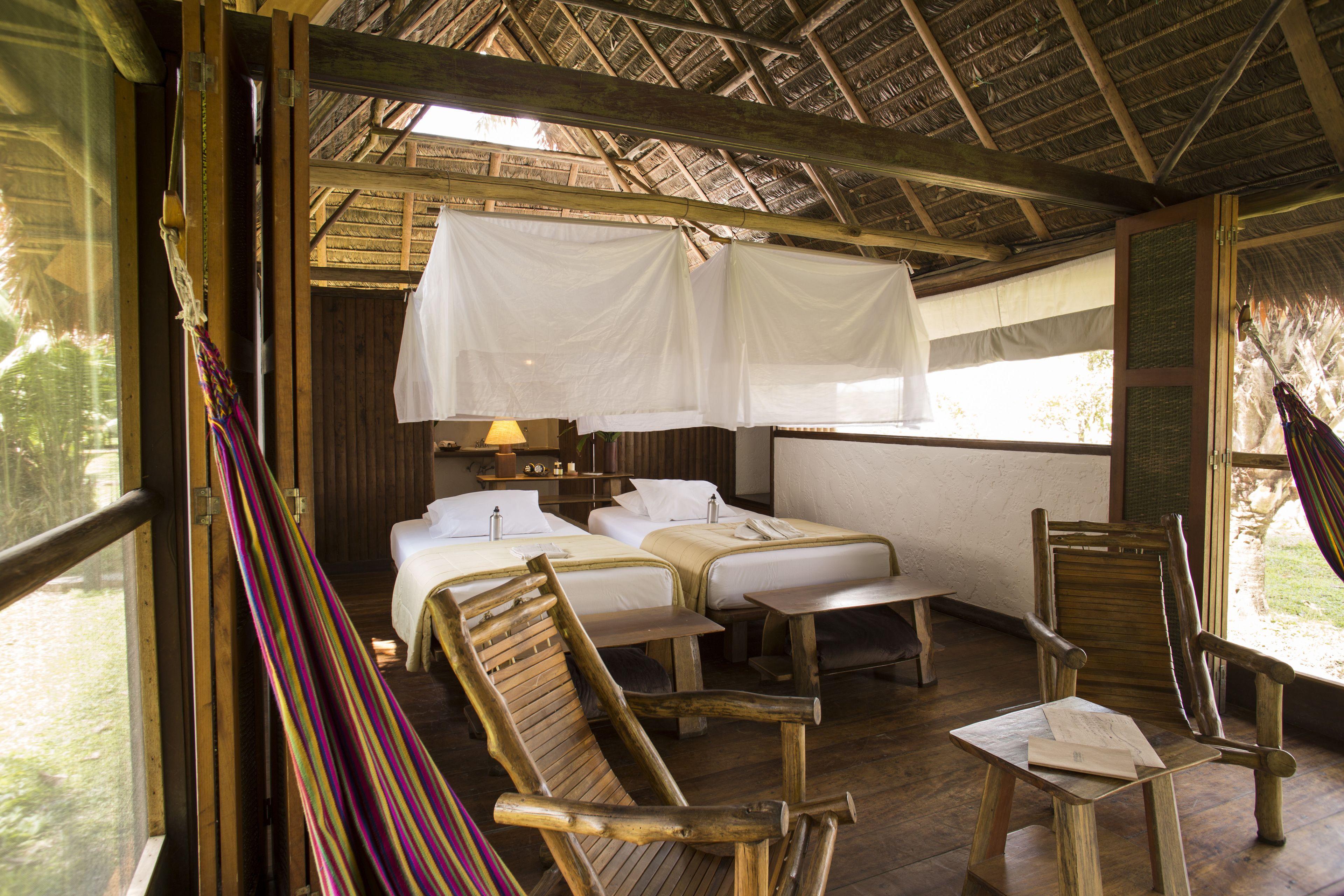 A room with two beds, a wooden chair, a small table, and a hammock.