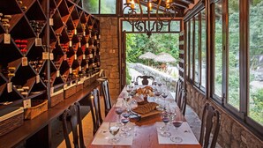 Una bodega con una larga mesa dispuesta para cenar, rodeada de estanterías llenas de vino y vistas al exterior.