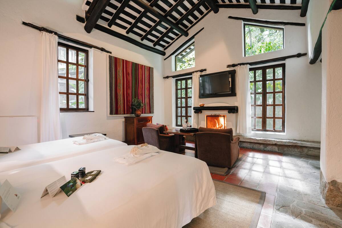 Une chambre d’hôtel avec deux lits, une cheminée, une télévision et de grandes fenêtres.