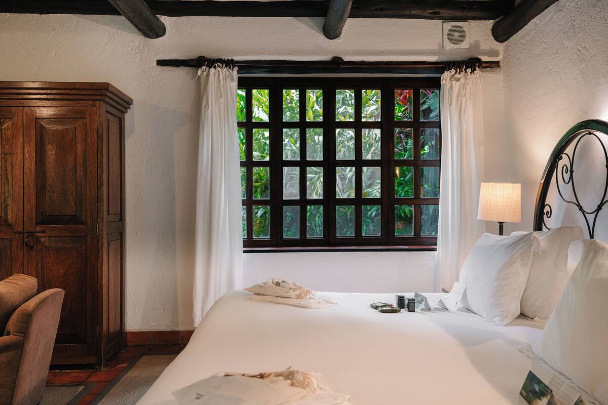 Une chambre à coucher avec un grand lit, une armoire en bois, une fenêtre avec des rideaux et une table de chevet avec une lampe.