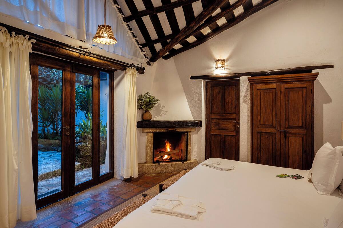 Une chambre avec une cheminée, des portes en bois et une grande fenêtre avec des rideaux.