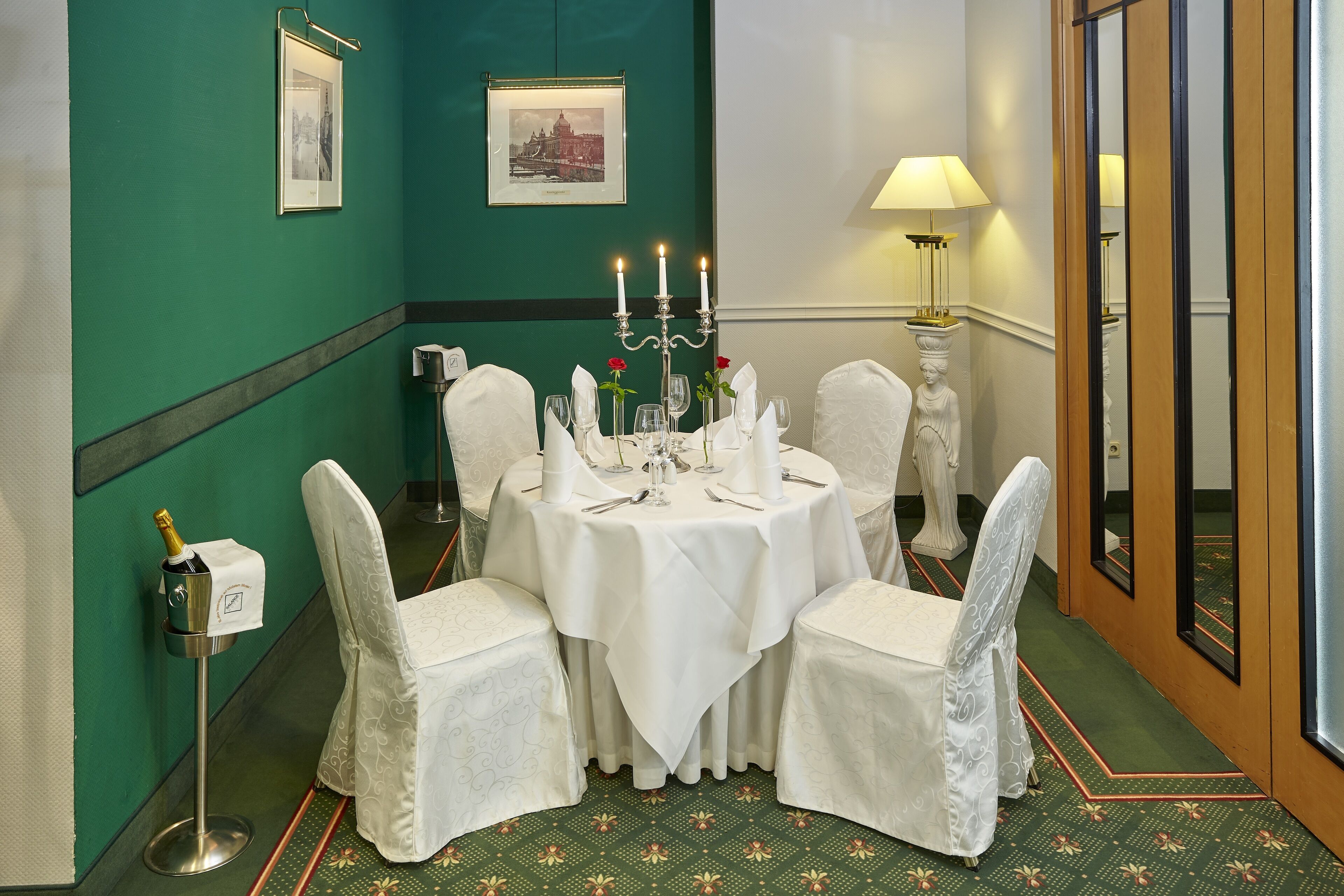 A dining area with a round table set for four, white chairs, a candelabra with candles, and a champagne bottle on a stand.