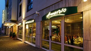 Um restaurante com um letreiro de neon verde, janelas amplas e rua de paralelepípedos.