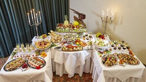 Mesa de buffet com diversos alimentos e um pássaro decorativo em um pedestal.