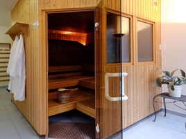Una sauna de madera con un banco, un perchero para toallas y una mesita con una planta.