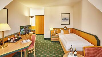 Habitación de hotel con cama, escritorio, silla, mesita de noche, lámpara, un cuadro en la pared y alfombra con estampado geométrico.