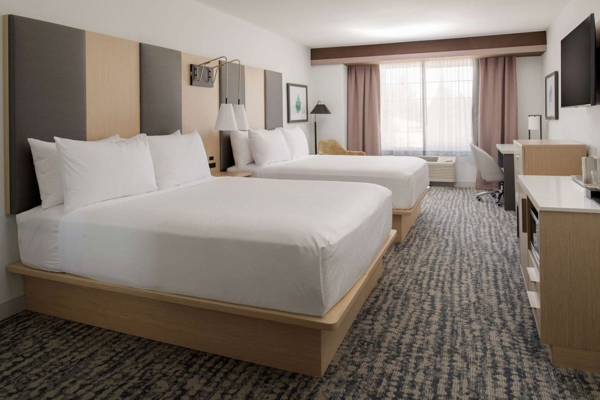 A hotel room with two beds, a desk, a chair, a TV, and a window with curtains.
