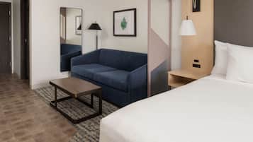 A hotel room with a bed, a sofa, a small table, a lamp, and a framed picture on the wall.
