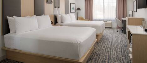 A hotel room with two beds, a desk, a chair, a TV, and a window with curtains.