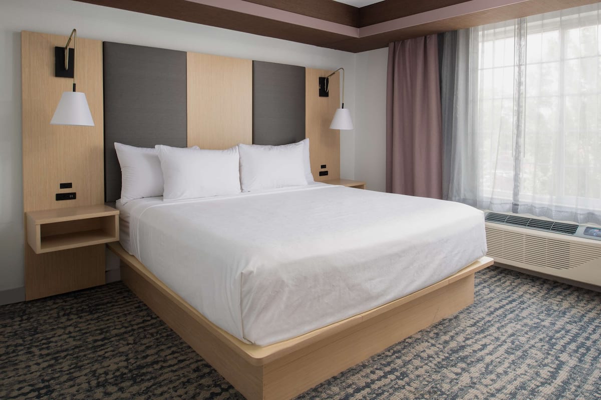 A hotel room with a large bed, two bedside tables, a headboard, and a window with curtains.