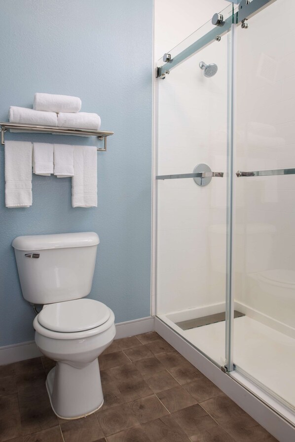 Un baño con inodoro, cabina de ducha de vidrio y toallero con toallas.