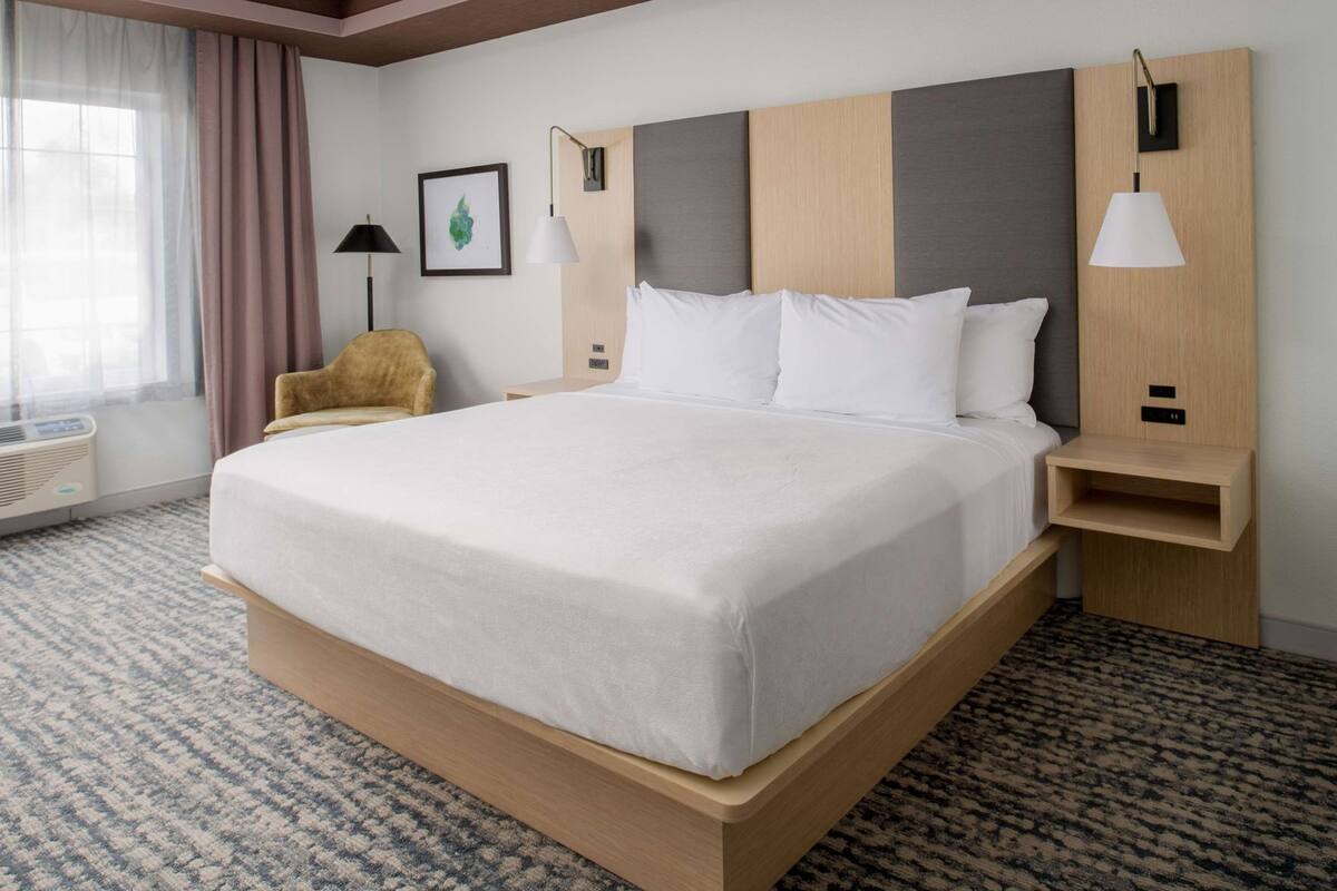 A hotel room with a large bed, a chair, a bedside table, a lamp, and a picture on the wall.