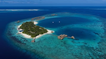 An aerial view of a tropical island resort with overwater bungalows, clear turquoise waters, and a small sandy beach.
