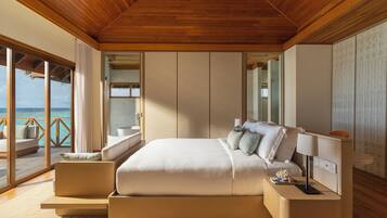Een ruime slaapkamer met een groot bed, een nachtkastje en uitzicht op de oceaan door middel van kamerhoge ramen.