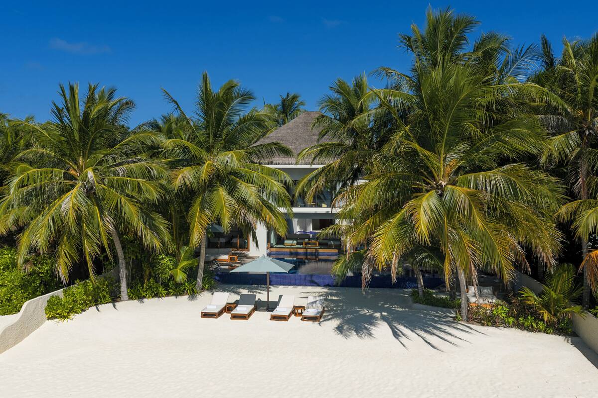 Ein Strandgrundstück mit Pool, Liegestühlen und Palmen.