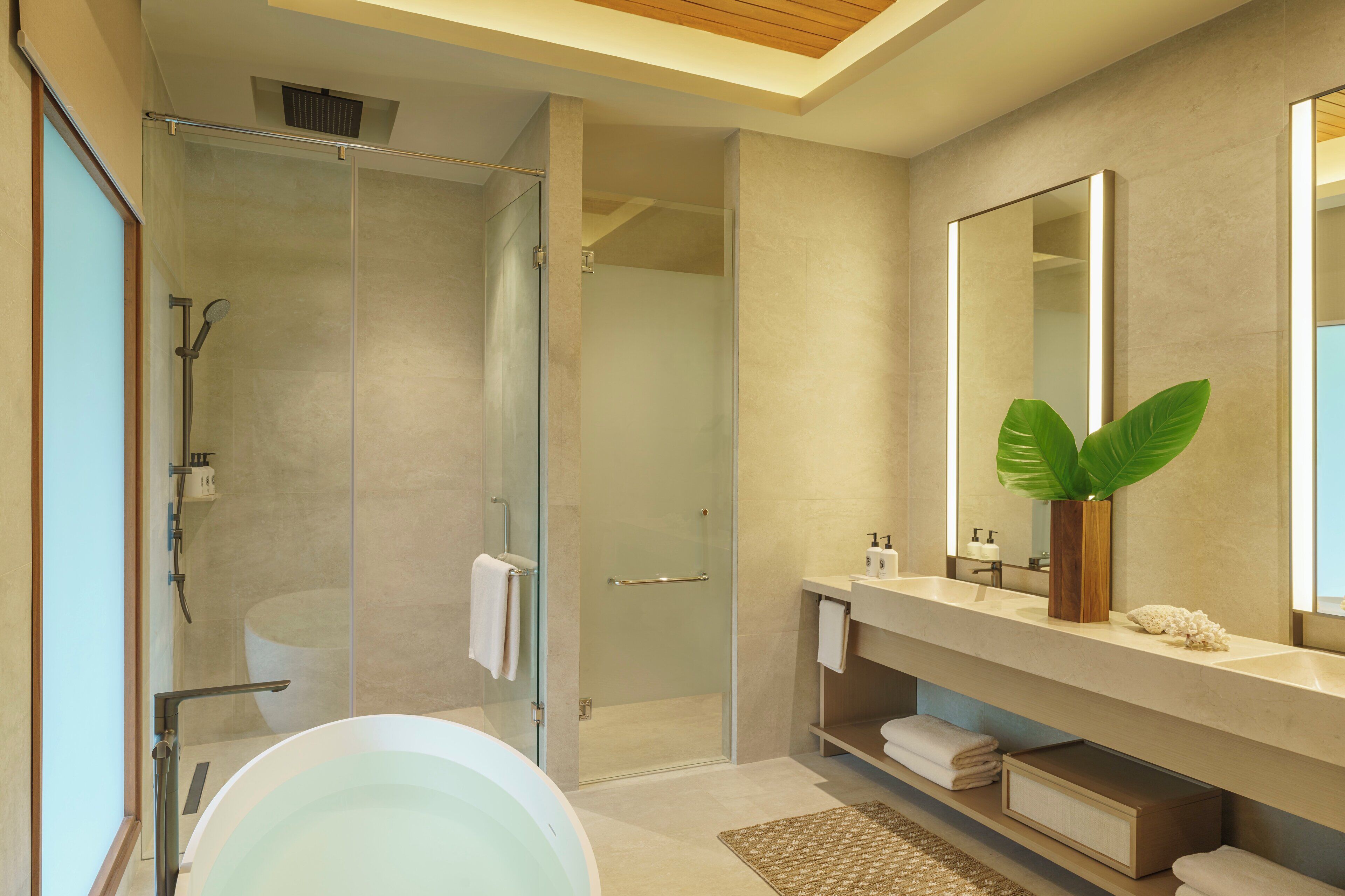 A modern bathroom with a glass-enclosed shower, a freestanding bathtub, and a vanity with a mirror and plant.