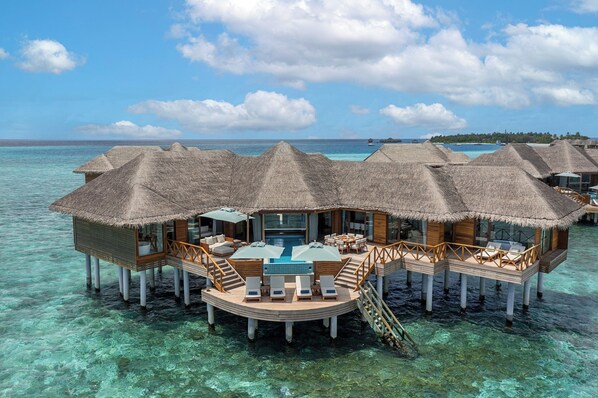 Bungalows sobre el agua con techos de paja, una piscina y un comedor.