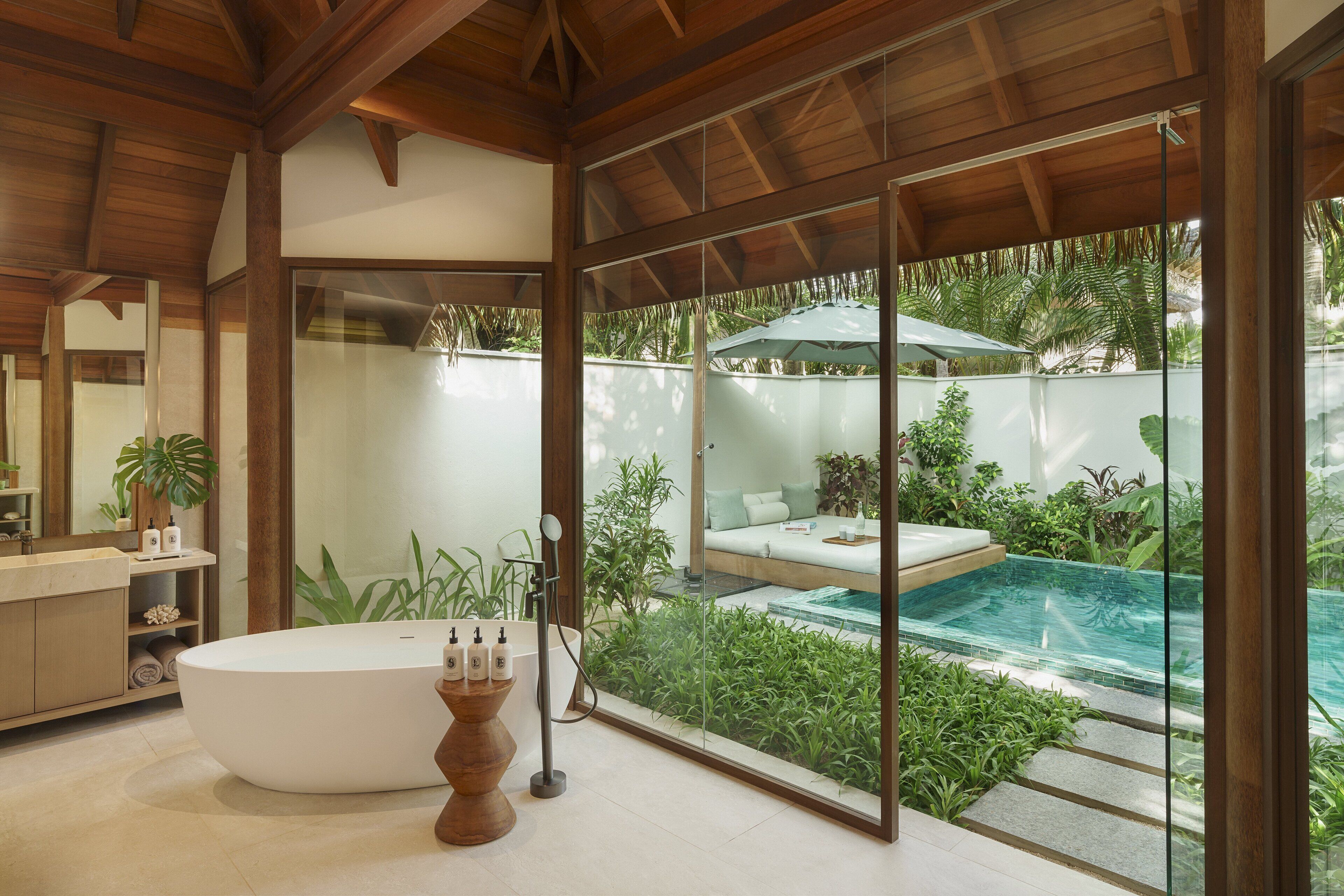 Un baño moderno con una bañera independiente, un espejo grande y vistas a un área de piscina exterior.