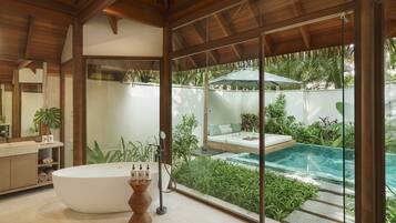 Un baño moderno con una bañera independiente, un espejo grande y vistas a un área de piscina exterior.