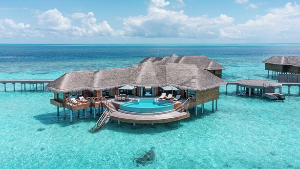 Overwater bungalows met een centraal zwembad, houten terras en rieten daken.
