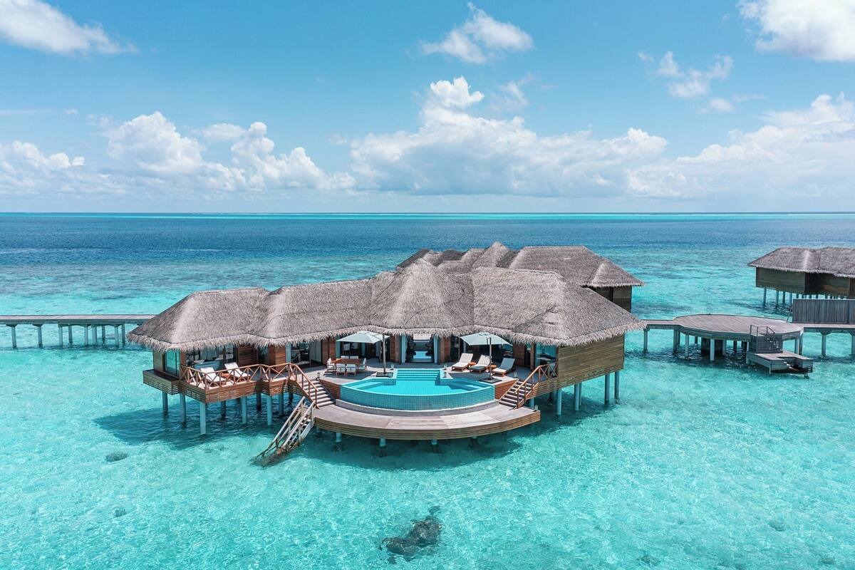 Wasserbungalows mit einem zentralen Pool, einer Holzterrasse und Reetdächern.