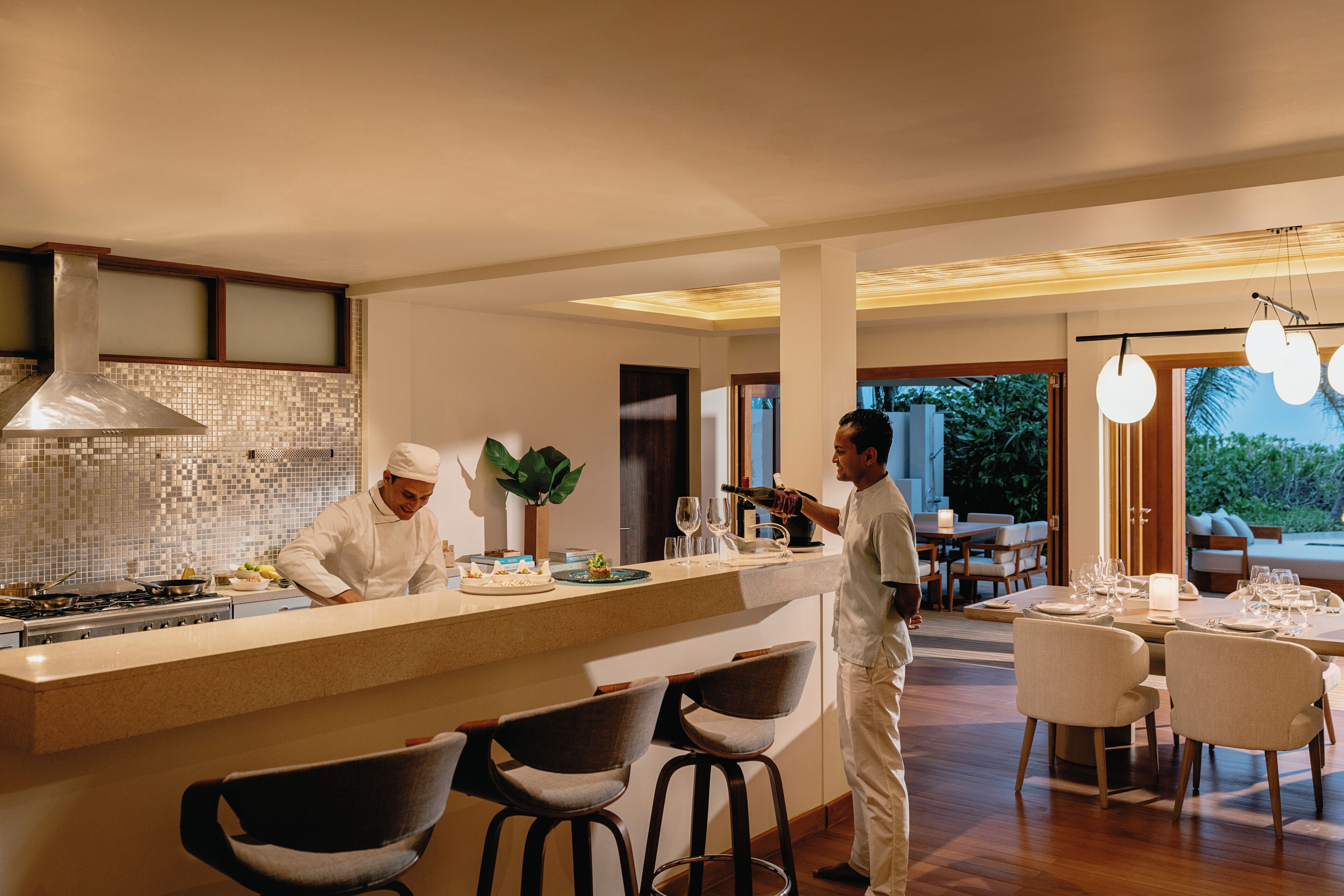 Una cucina moderna con uno chef che prepara cibo, un'area pranzo con un tavolo e sedie ampie e vista sull'esterno.