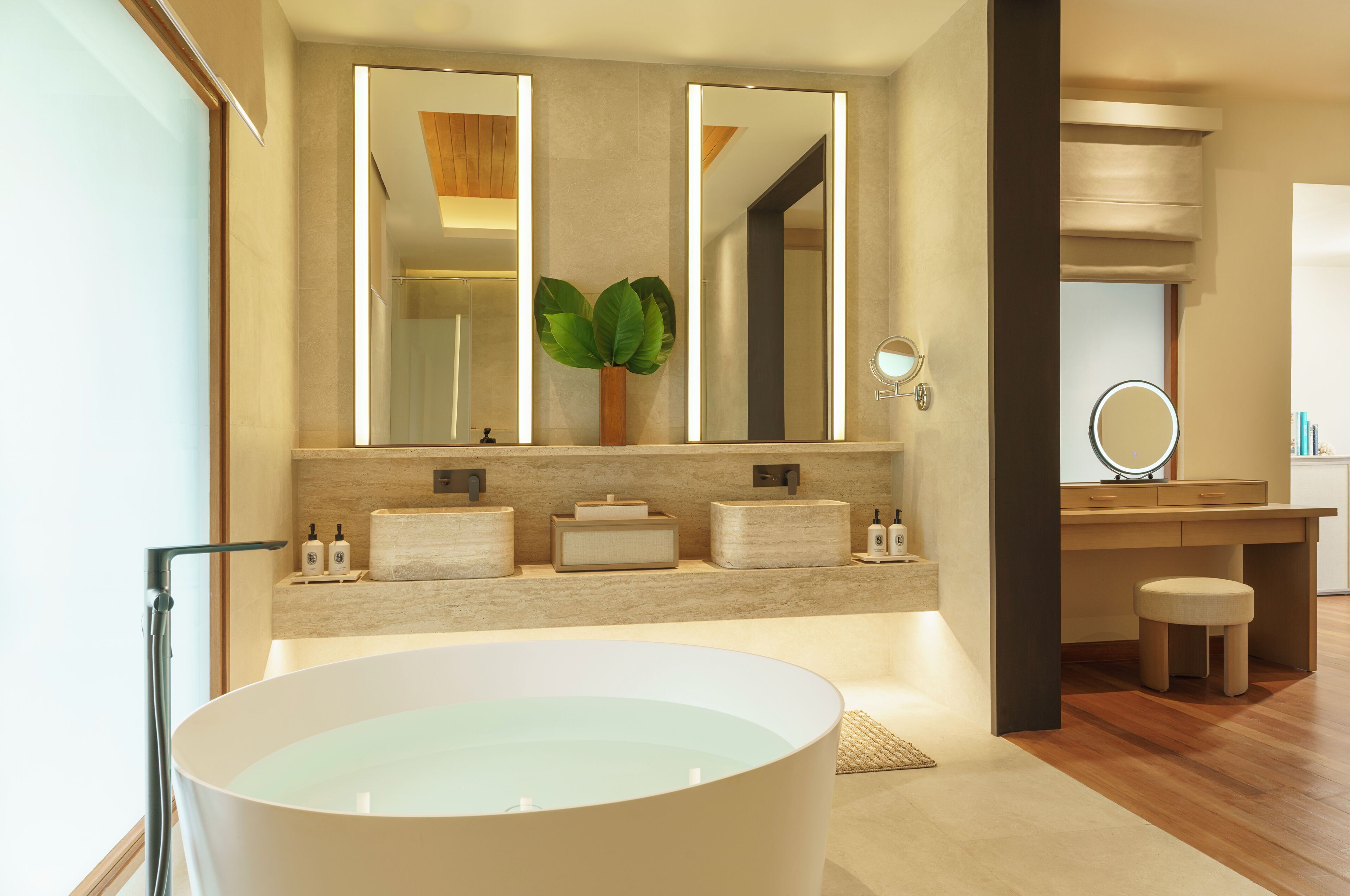 Ein modernes Badezimmer mit einer großzügigen, freistehenden Badewanne, einem Waschtisch mit Spiegel und einem Blumentopf.