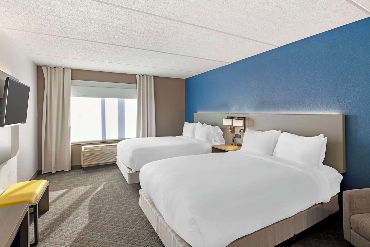 A hotel room with two beds, a TV, a desk, and a window with curtains.