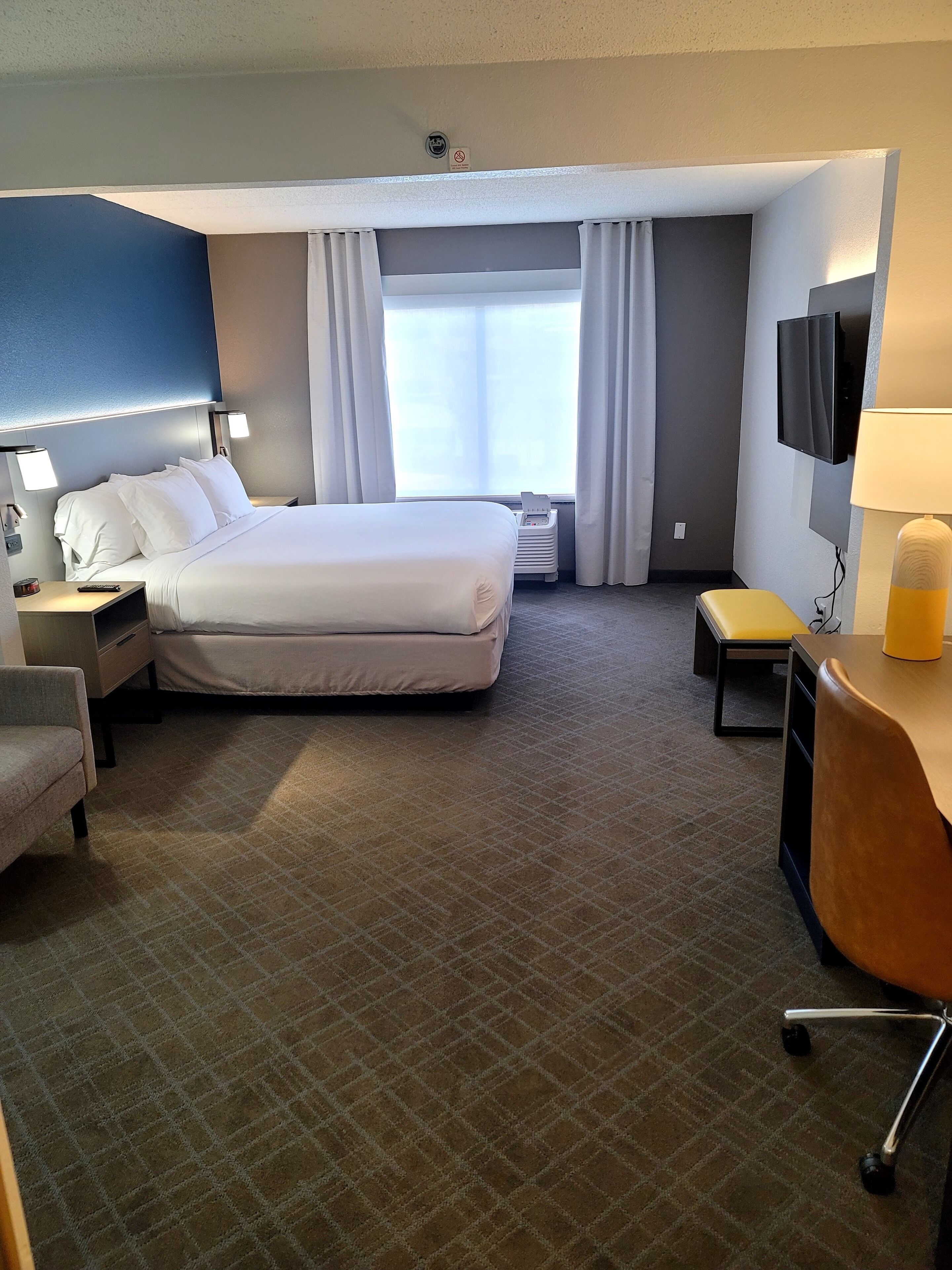 Habitación de hotel con una cama grande, un escritorio, una silla, un televisor y una ventana con cortinas.