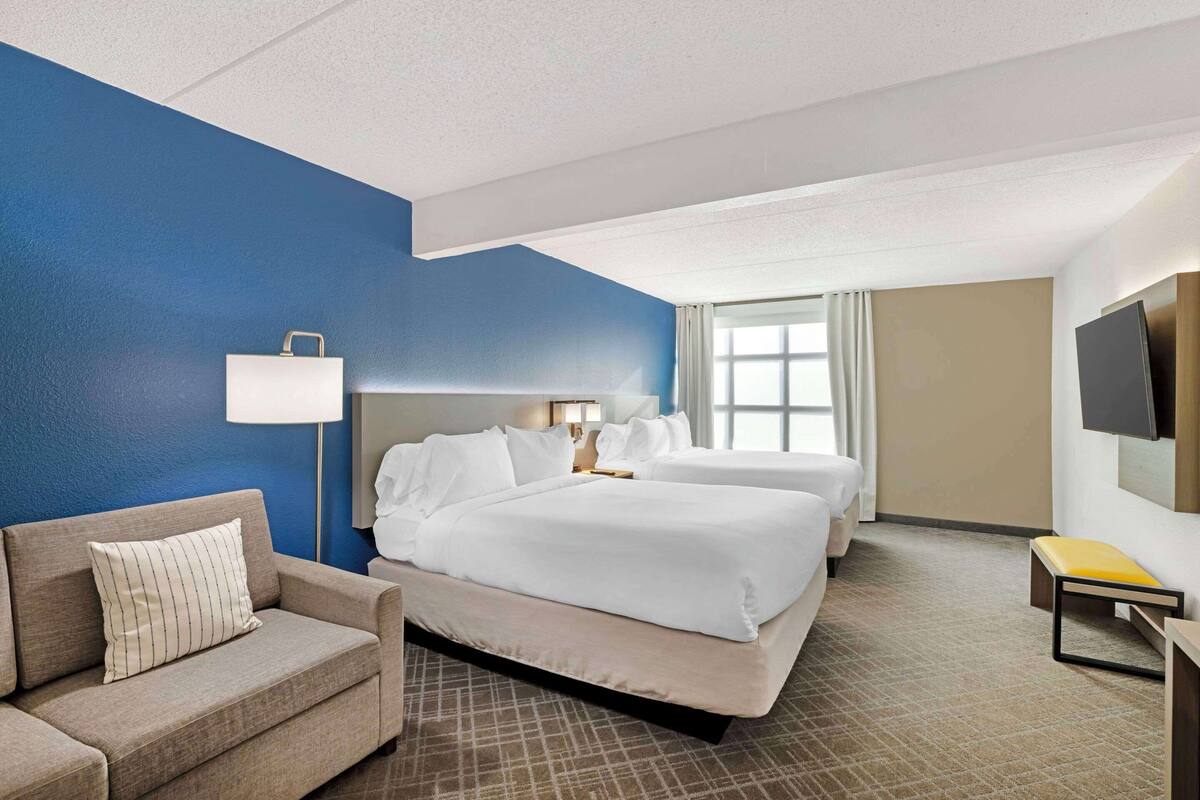 A hotel room with a large bed, a smaller bed, a sofa, a TV, and a window with curtains.