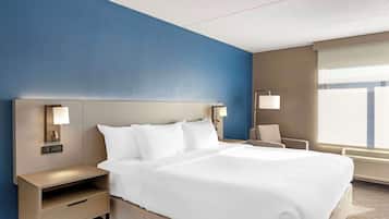 Una habitación de hotel con una cama grande, una mesita de noche, una silla y una ventana con persianas.