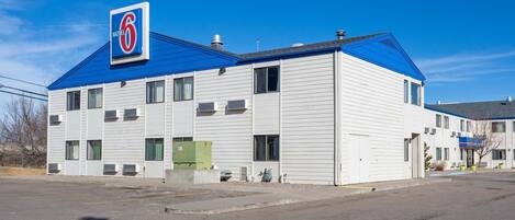 Un edificio de motel de 6 habitaciones con techo azul, revestimiento blanco y múltiples ventanas.