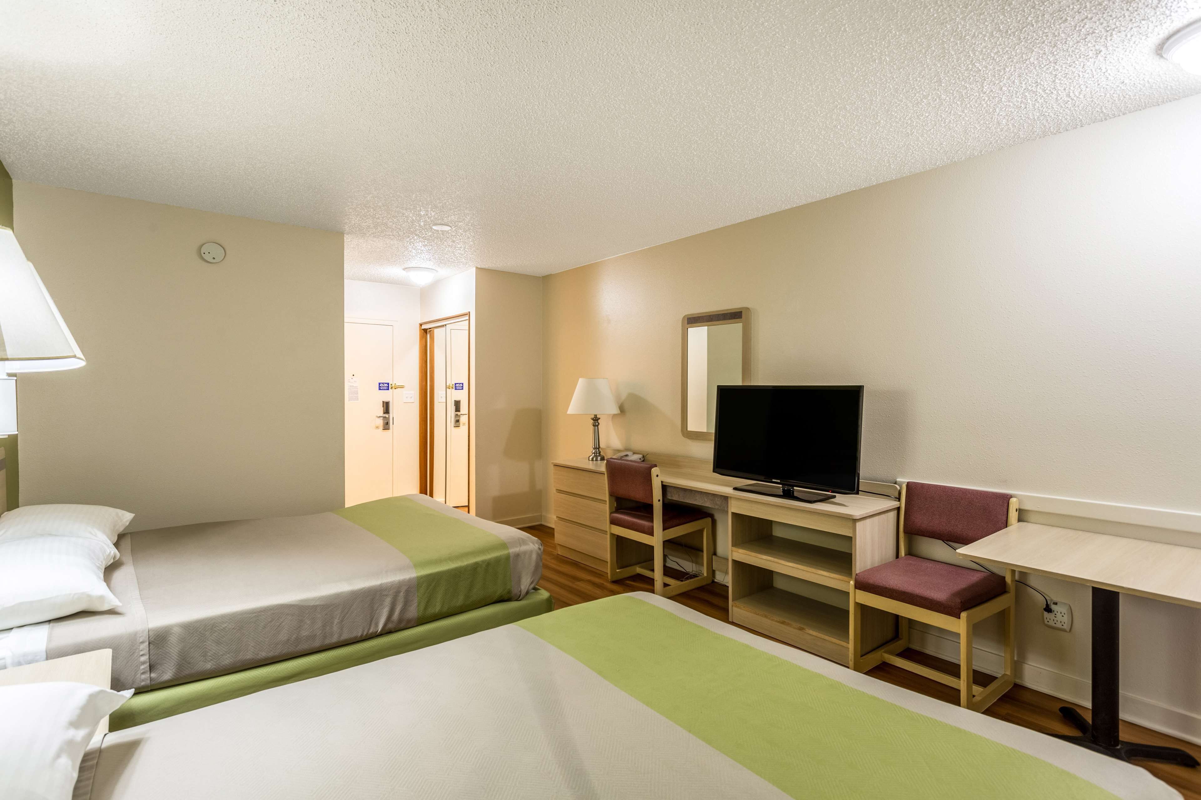 A hotel room with two single beds, a desk with a chair, a television, and a mirror.