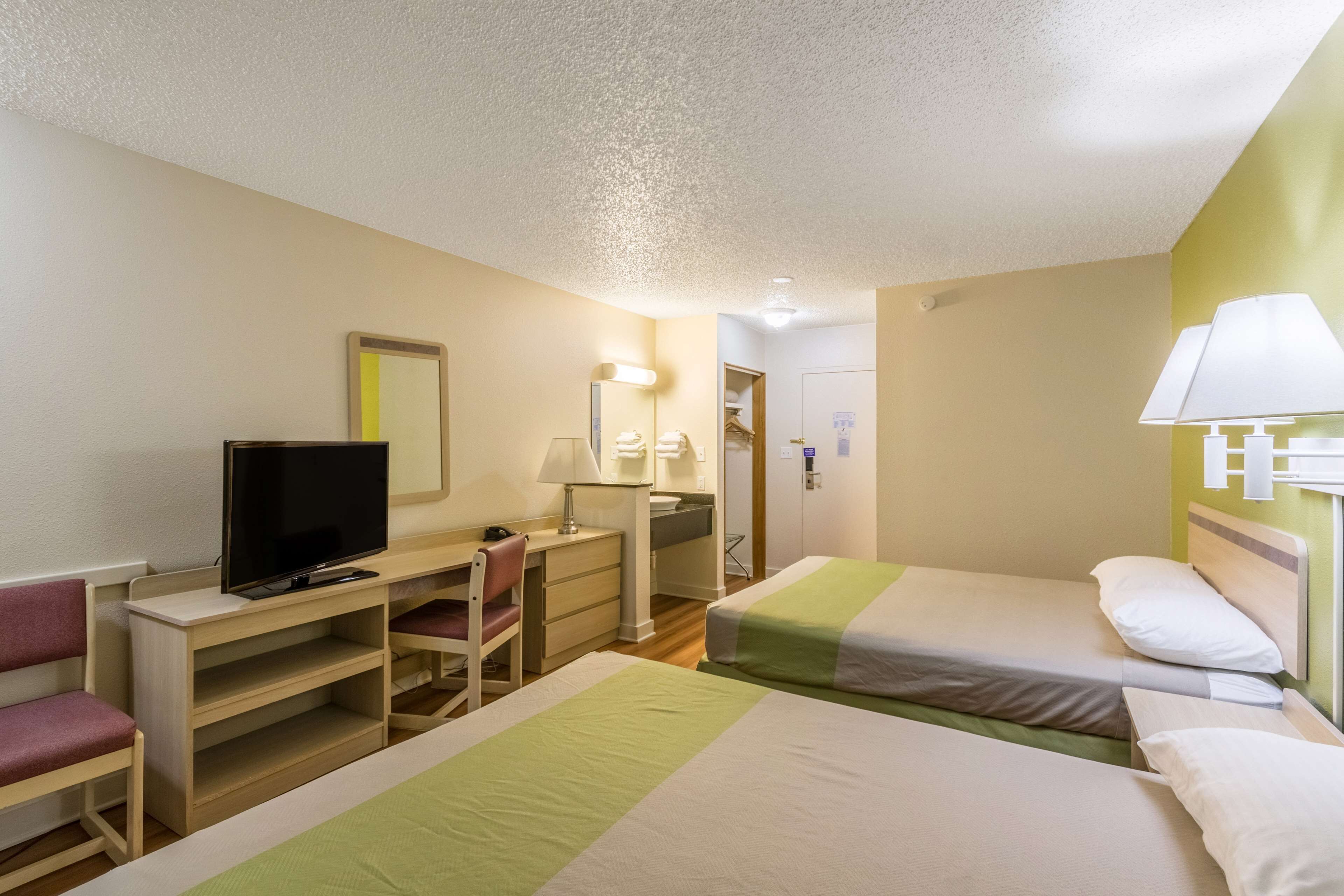 Une chambre d’hôtel avec deux lits, un bureau avec une télévision, une chaise et un miroir.