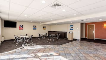 A spacious indoor area with a tiled floor, several tables and chairs, a flat-screen TV mounted on the wall, and a door with a number sign.